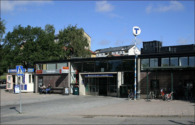 Hsselby Strand, Grne Linien (T19). Dies ist die westliche Endstation des ersten Teilsystems der Stockholmer Tunnelbana. Diese Teilsystem (Grne Linien) verkehrt weitgehend oberirdisch, meist in Dammlage. Die Innenstadtbereiche werden unterirdisch durchfahren. Teilweise wurde die Trasse im Straenbahnvorlauf betrieben und spter auf U-Bahnbetrieb umgebaut. Erkennbar sind die Zugnge der Stockholmer U-Bahn an dem blauen T auf weiem Grund. Am 19.11.1958 erreichte die U-Bahn Hsselby. 25.08.2007 (Matthias)